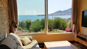 Una sala de estar con un amplio ventanal que ofrece vistas al mar y a las colinas.