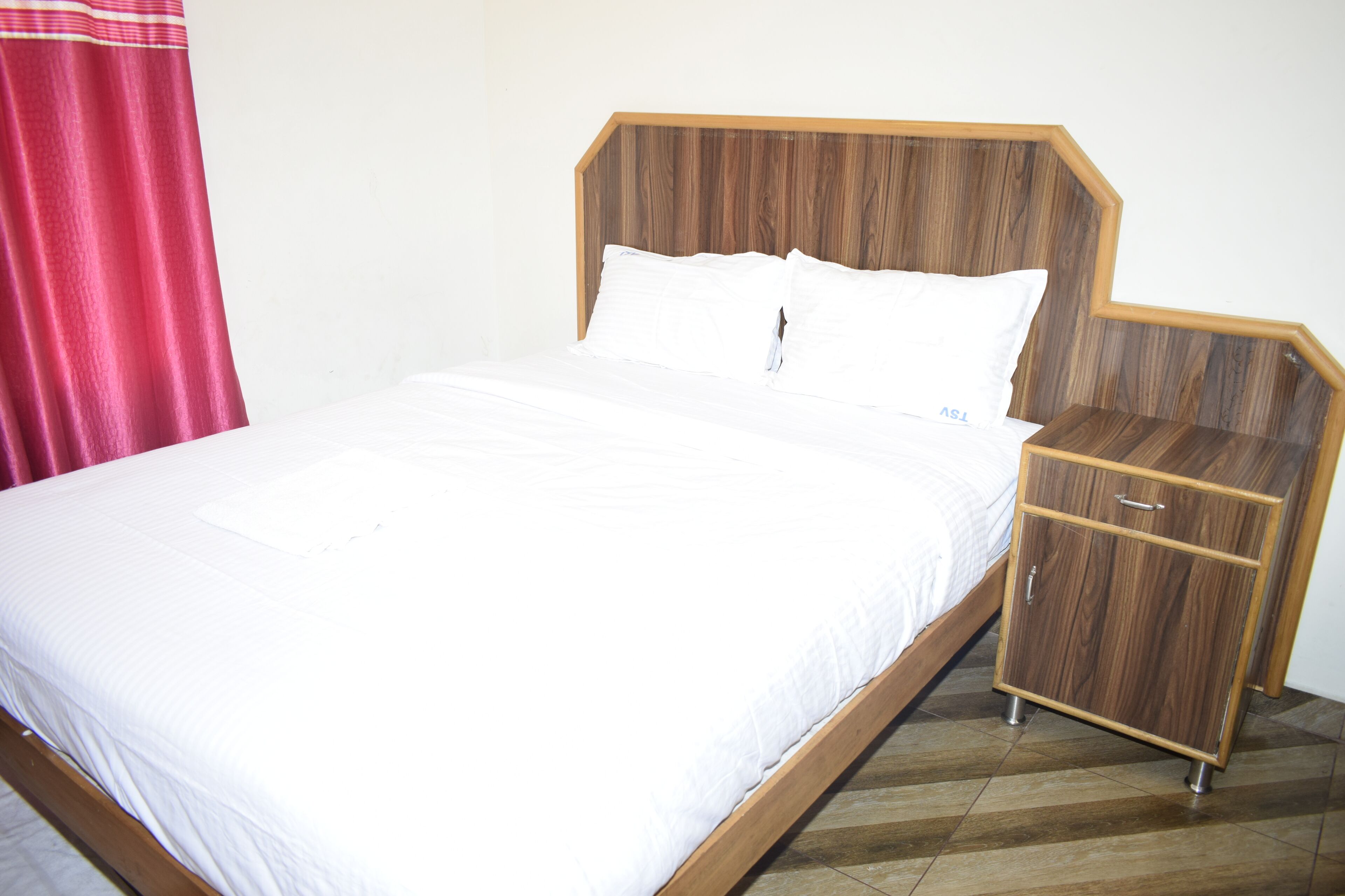 Una cama con cabecera de madera, una mesita de noche y una cortina roja.