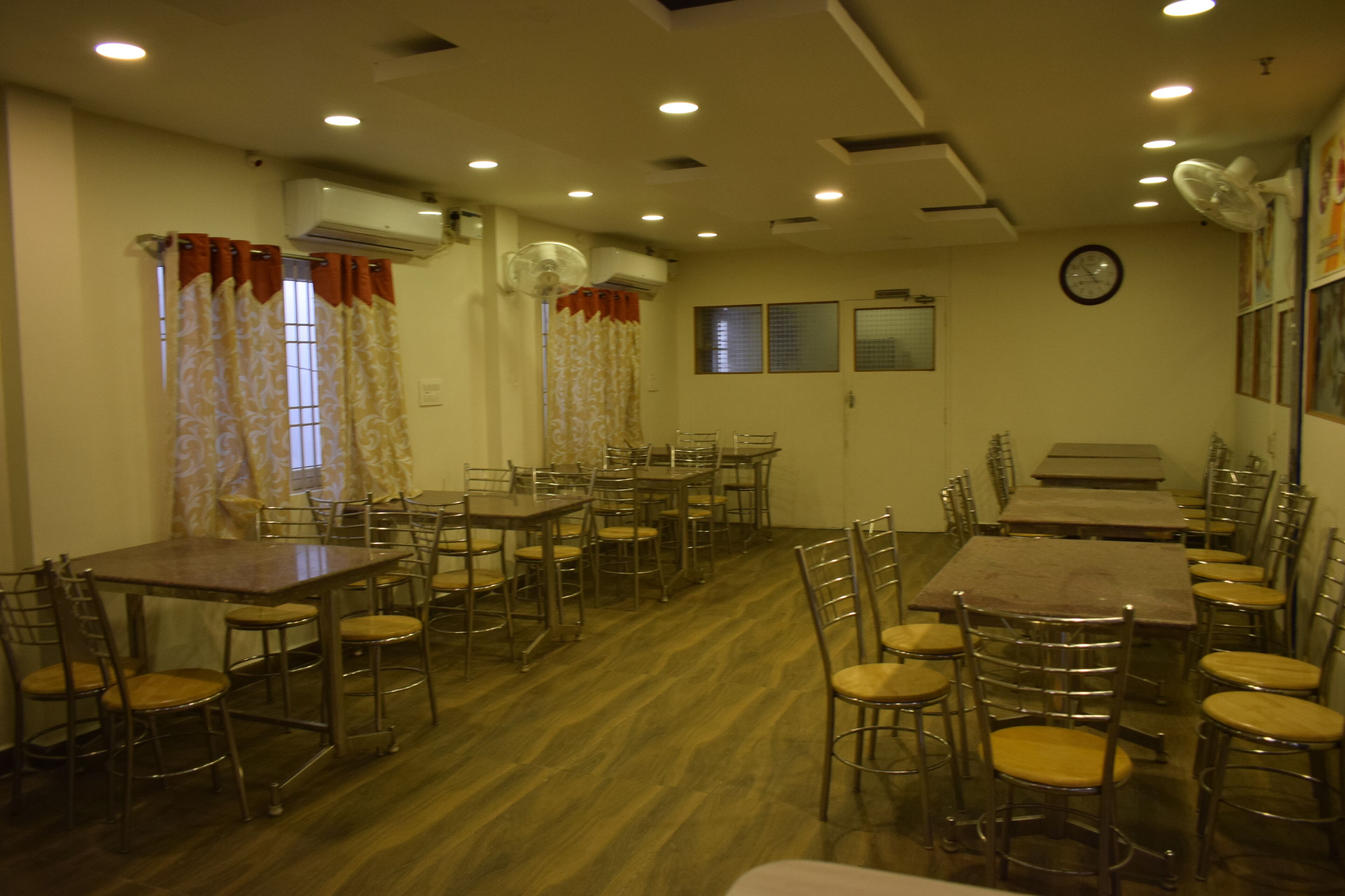 A dining area with multiple tables and chairs, an air conditioning unit, and a clock on the wall.