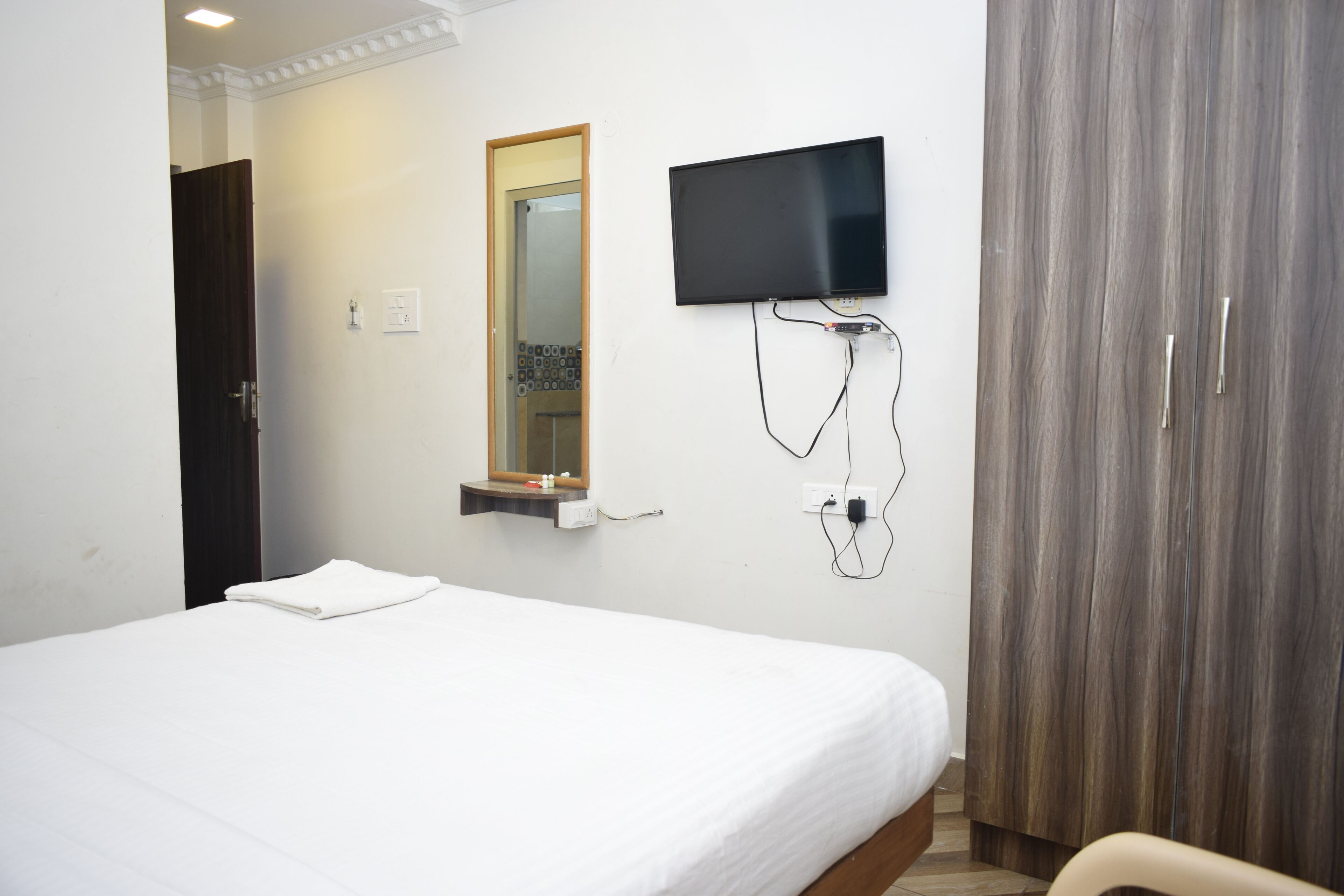 A hotel room with a bed, a television mounted on the wall, a mirror, and a wardrobe.