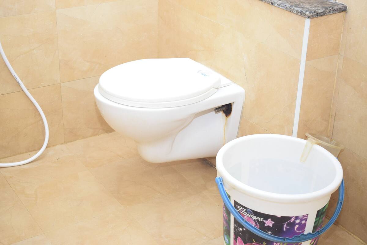 A toilet with a white lid and a bucket with a floral design next to it.