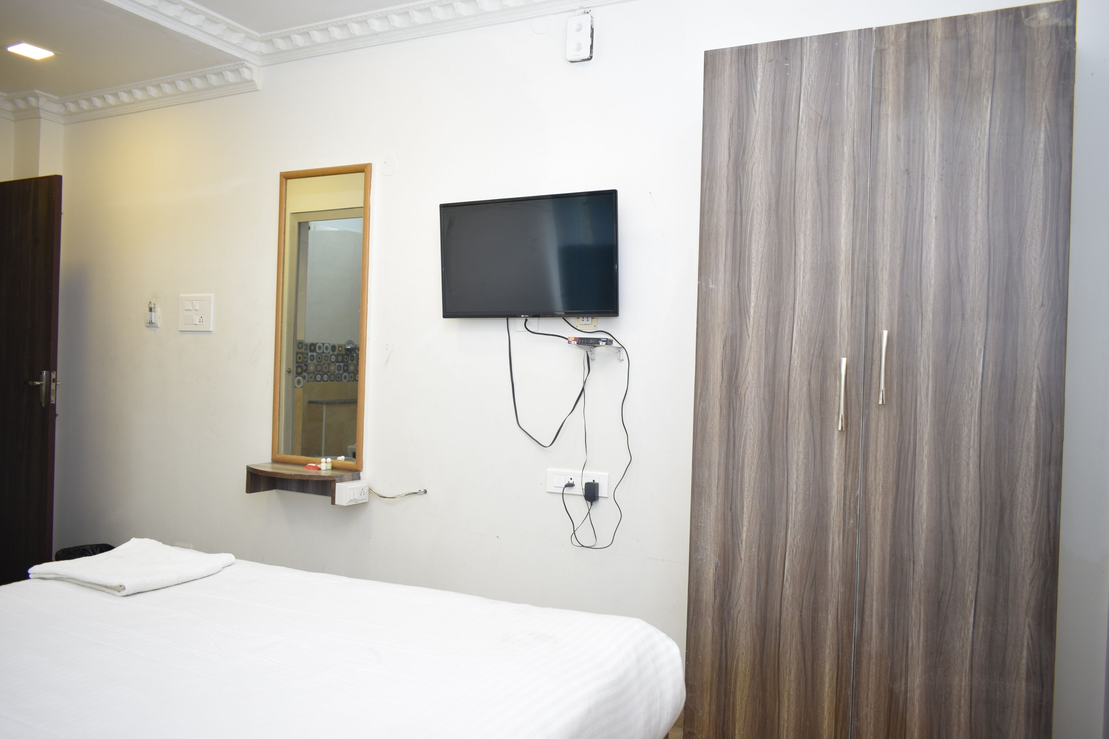 A hotel room with a bed, a TV mounted on the wall, and a wardrobe.