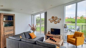 Un salón moderno con sofá, mesa de centro, televisor y una silla. Hay un mueble de madera y un adorno en la pared.