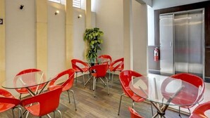 Een vergaderruimte met rode stoelen en een glazen tafel, houten vloeren en een plant in het midden.