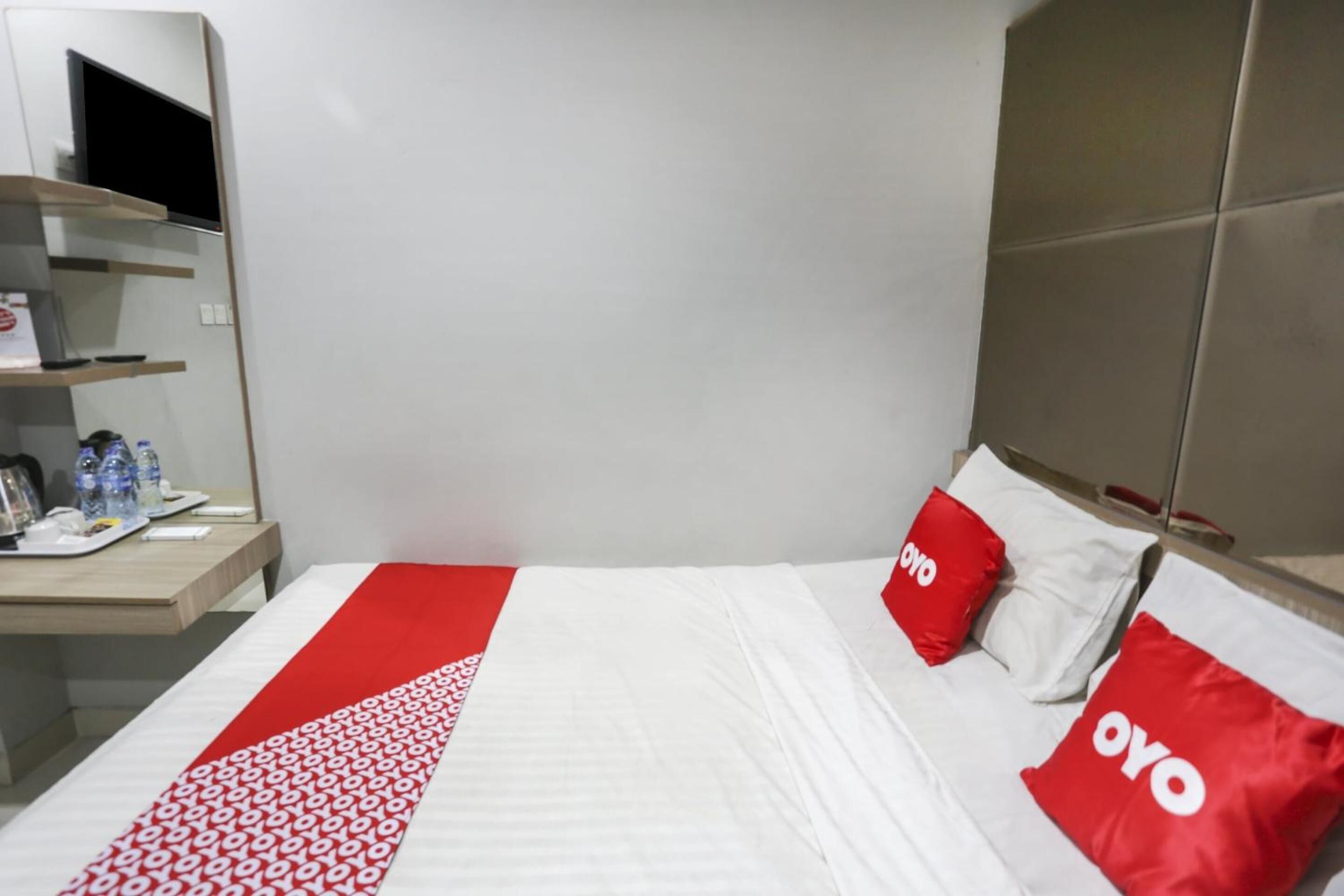 A hotel room with a bed, a desk with a computer, and a TV on a shelf.
