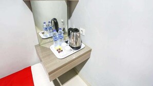Hotelkamer met een houten bureau, een spiegel, een waterkoker en een dienblad met waterflessen en bekers.