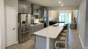 A modern kitchen with stainless steel appliances, a central island, and a dining area with a view of the outdoors. - Brand New Luxury Property at The Peninsula- Double Master Sleeps 10 (Millsboro)