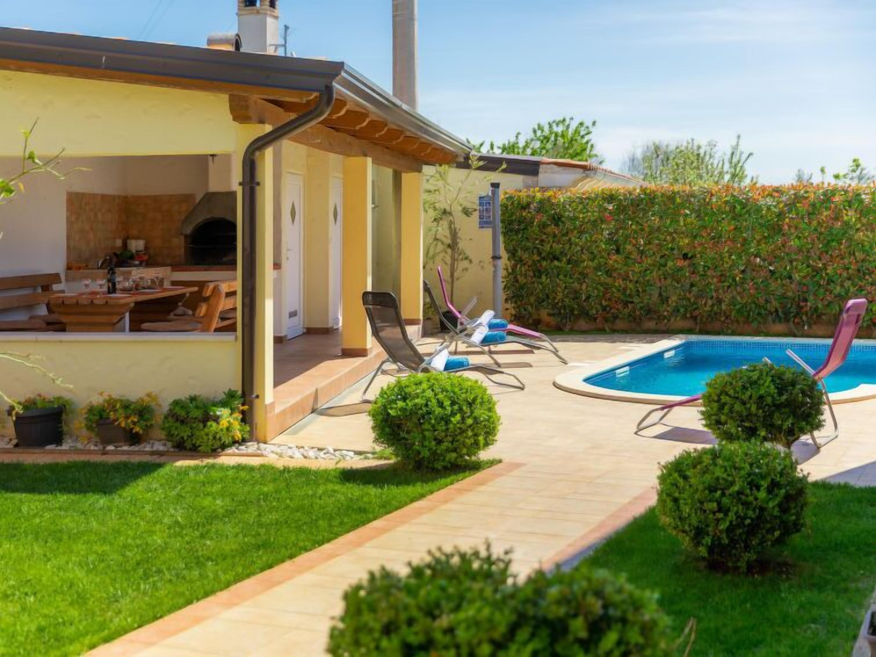 A modern outdoor patio with a pool, lounge chairs, and a barbecue area.