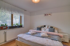 Quarto bem arrumado com uma cama, mesas de cabeceira, radiador e plantas em vasos junto à janela.