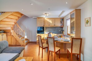 A modern kitchen with wooden cabinets, a dining area with chairs, and a staircase.