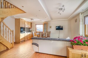 A modern kitchen with wooden cabinets, a dining area with a table and chairs, a TV mounted on the wall, and a staircase leading to another level. - Pool & Wellness Chalet Sunshine, Vransko, Slovenia (Vransko)