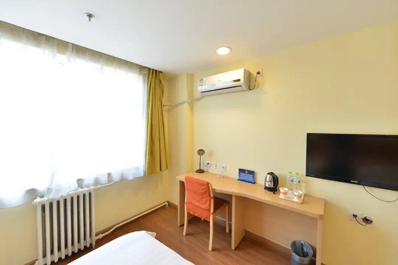 Une chambre d’hôtel équipée d’un lit, d’un bureau, d’une chaise, d’un climatiseur, d’une télévision et d’une fenêtre avec des rideaux.
