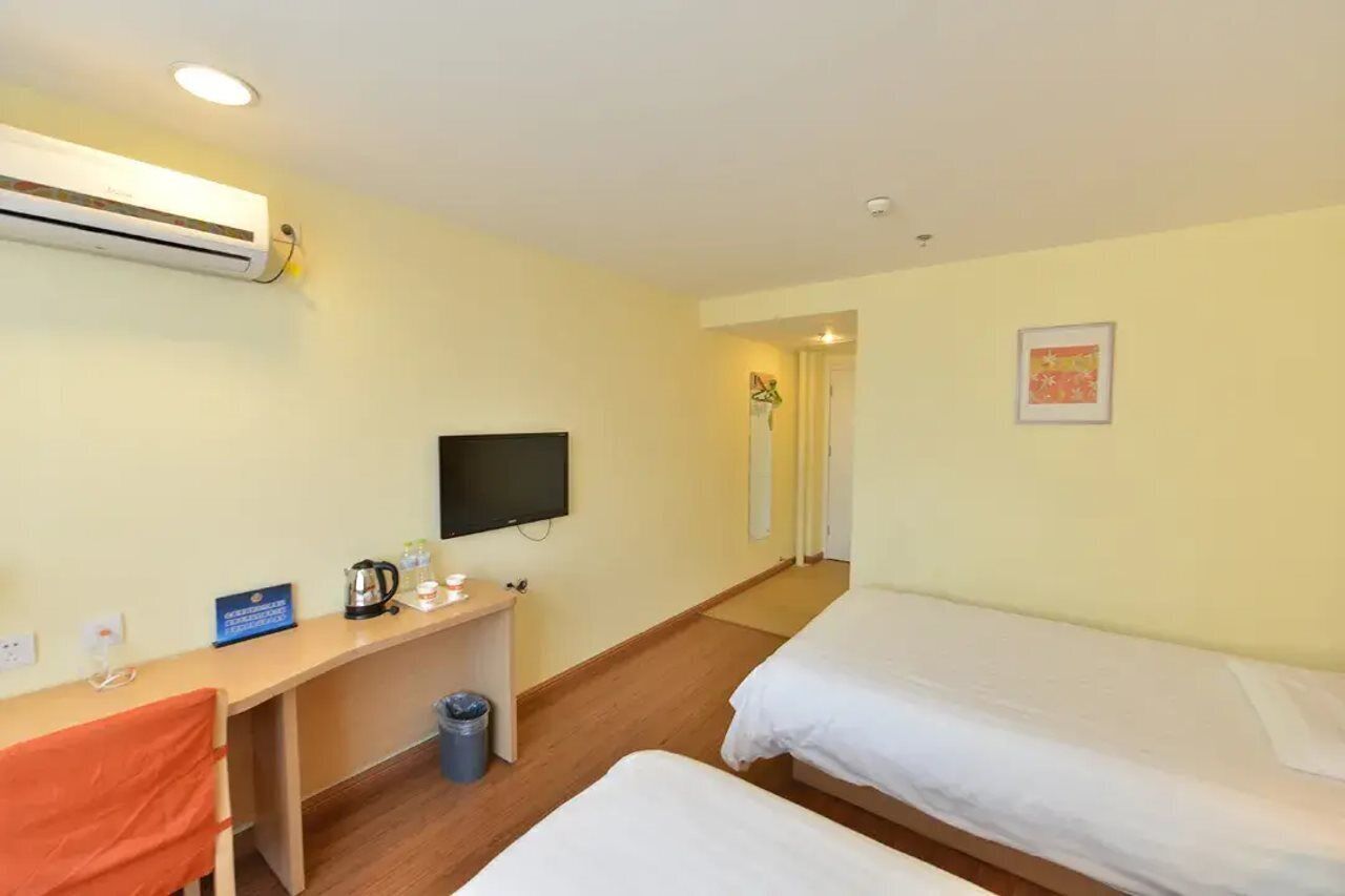 A hotel room with two beds, a desk with a television, a coffee maker, and a trash bin.