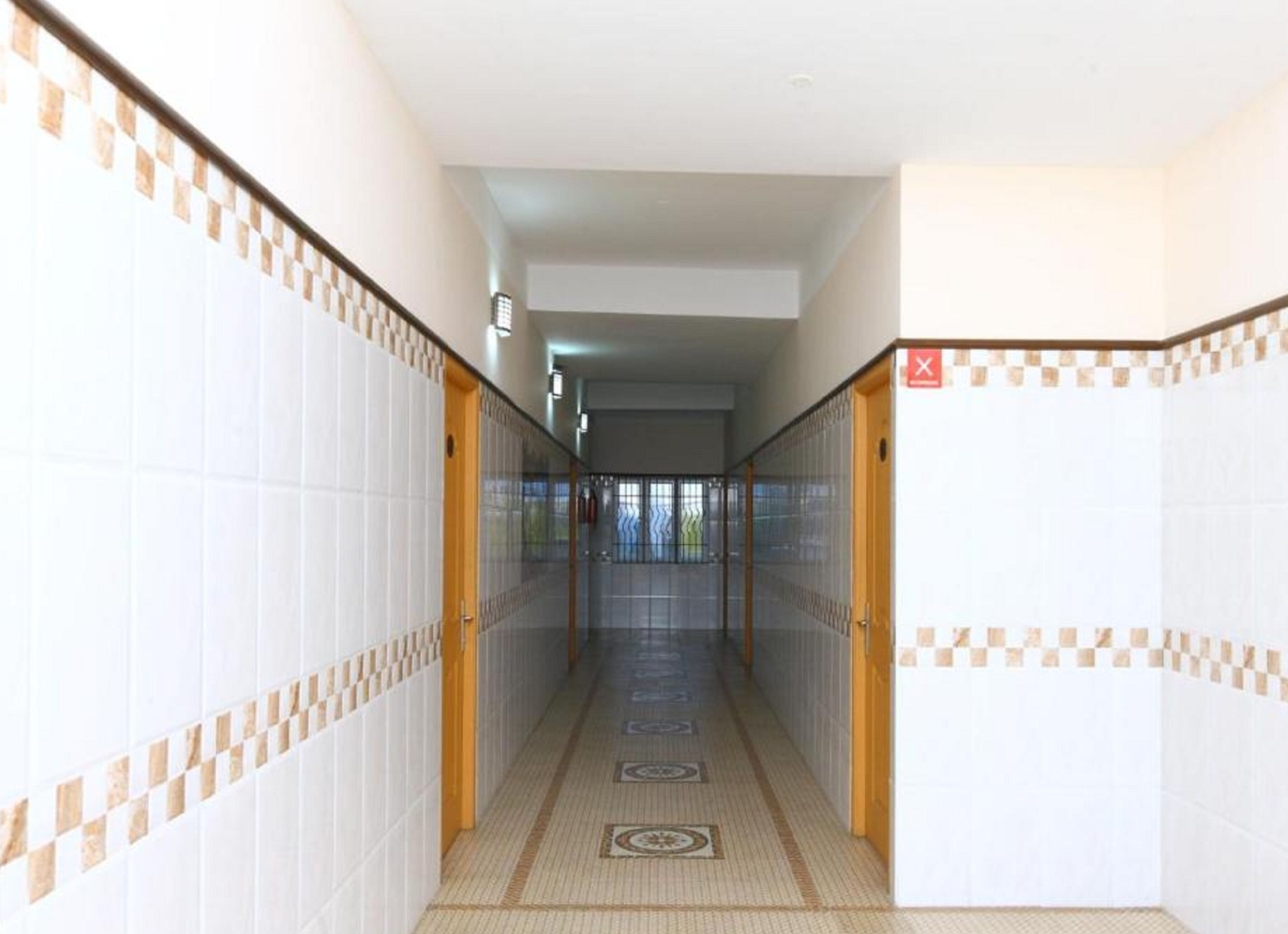 A corridor with tiled walls and a patterned floor, leading to a door with a red 'X' sign.