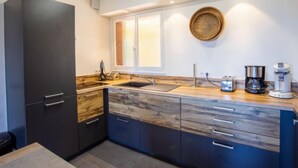 Eine moderne Küche mit dunklen Schränken, einer Holzausziehtheke, einem Spülbecken, einem Fenster mit Jalousien und einer Kaffeemaschine.