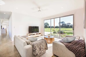 A modern living room with a sofa set, a television, and a large window offering a view of a green landscape.