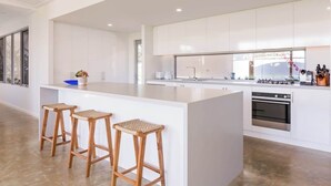 Una cocina moderna con armarios blancos, una isla central con taburetes y un amplio ventanal que proporciona luz natural.
