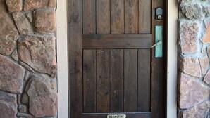 A wooden door with a 'No Smoking' sign, set in a stone wall with a doormat and a wall-mounted light fixture. - Aspen Stash Pad Steps From The Slopes (Aspen)