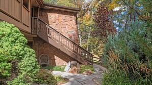 A stone staircase leading to a wooden deck with a stone wall, surrounded by greenery and trees. - Aspen Stash Pad Steps From The Slopes (Aspen)