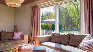 A cozy living room with a large window, a sofa, a coffee table, and a bookshelf. - Lake House - Pomeranian-style house by the lake with a lake view, sauna, fireplace, and rowboat (Luckow)