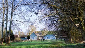A house with a blue exterior, surrounded by a grassy yard and trees. - Lake House - Pomeranian-style house by the lake with a lake view, sauna, fireplace, and rowboat (Luckow)