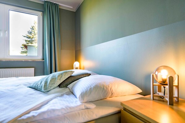 A neatly made bed with pillows, a bedside lamp, and a window with curtains.