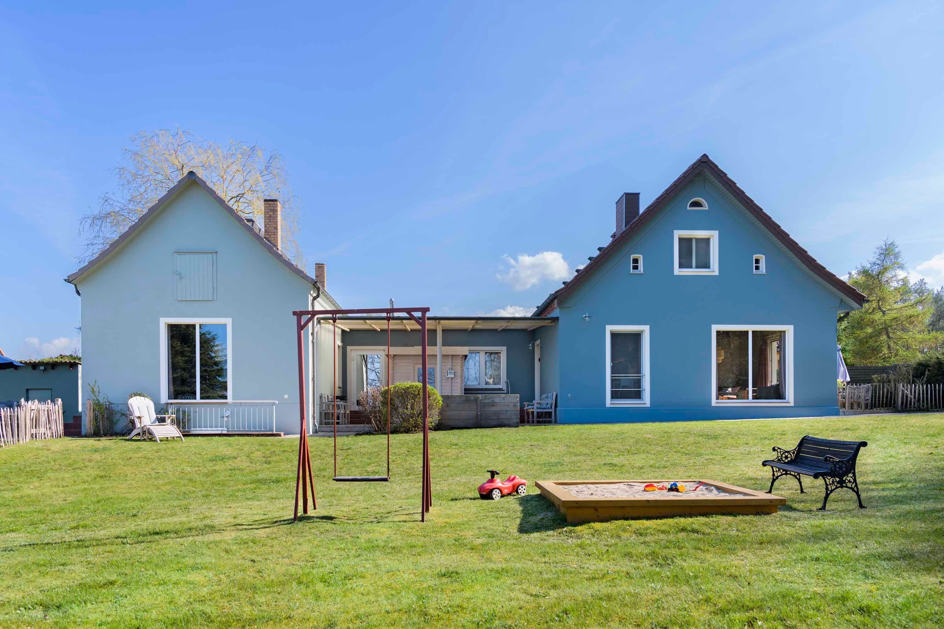 Une maison à deux étages avec un porche, une balançoire, un bac à sable et un banc.