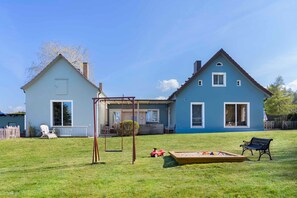 Une maison à deux étages avec un porche, une balançoire, un bac à sable et un banc.