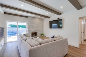 A living room with a sectional sofa, a fireplace, a flat-screen TV, and a large window.