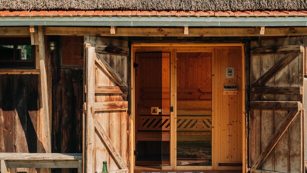 Un edificio in legno con un'ampia porta aperta, una panchina all'esterno e una bottiglia verde a terra.