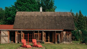 Un rustico fienile con tetto di paglia, porte in legno e un portico coperto con poltrone Adirondack rosse.
