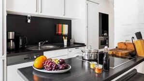 A modern kitchen with white cabinets, a black countertop, and a variety of appliances including a coffee maker, a kettle, and a microwave. - Pommernhaus Vorsee am Kiefernwald Kamin Boot - Thatched half-timbered house, fireplace (Ahlbeck)