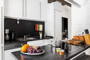 A modern kitchen with white cabinets, a black countertop, and a variety of appliances including a coffee maker, a kettle, and a microwave.