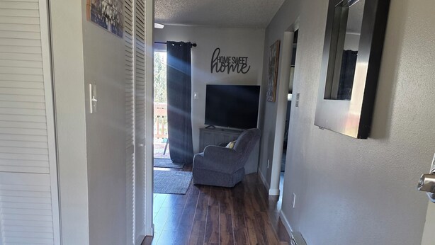 A hallway with a wooden floor, a gray wall with a 'HOME SWEET HOME' sign, a gray chair, and a TV. - Lee's Helena Hideout (Helena)