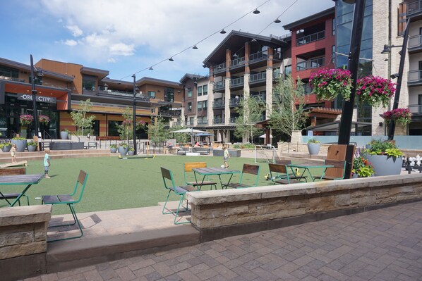 Un espace extérieur aménagé en terrasse, avec des chaises et des tables vertes, entouré d’immeubles dotés de balcons et de jardinières suspendues.