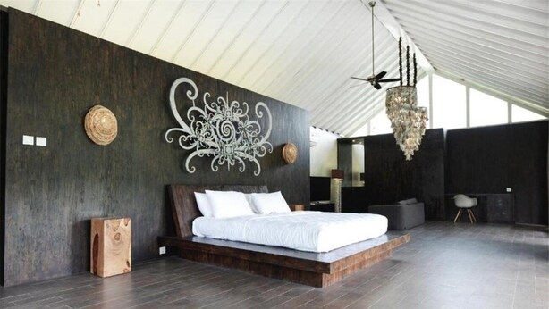 A modern bedroom with a large bed, dark wooden walls, and a decorative wall piece. - Sandhya Villa Ubud (Payangan)
