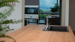 A modern kitchen with a wooden countertop, stainless steel appliances, and a view of the sea. - The Bridge Luxury Villa (Nha Trang)