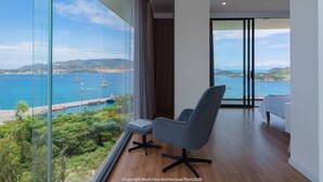 A modern room with a large glass window, a grey chair, a wooden floor, and a bed. - The Bridge Luxury Villa (Nha Trang)