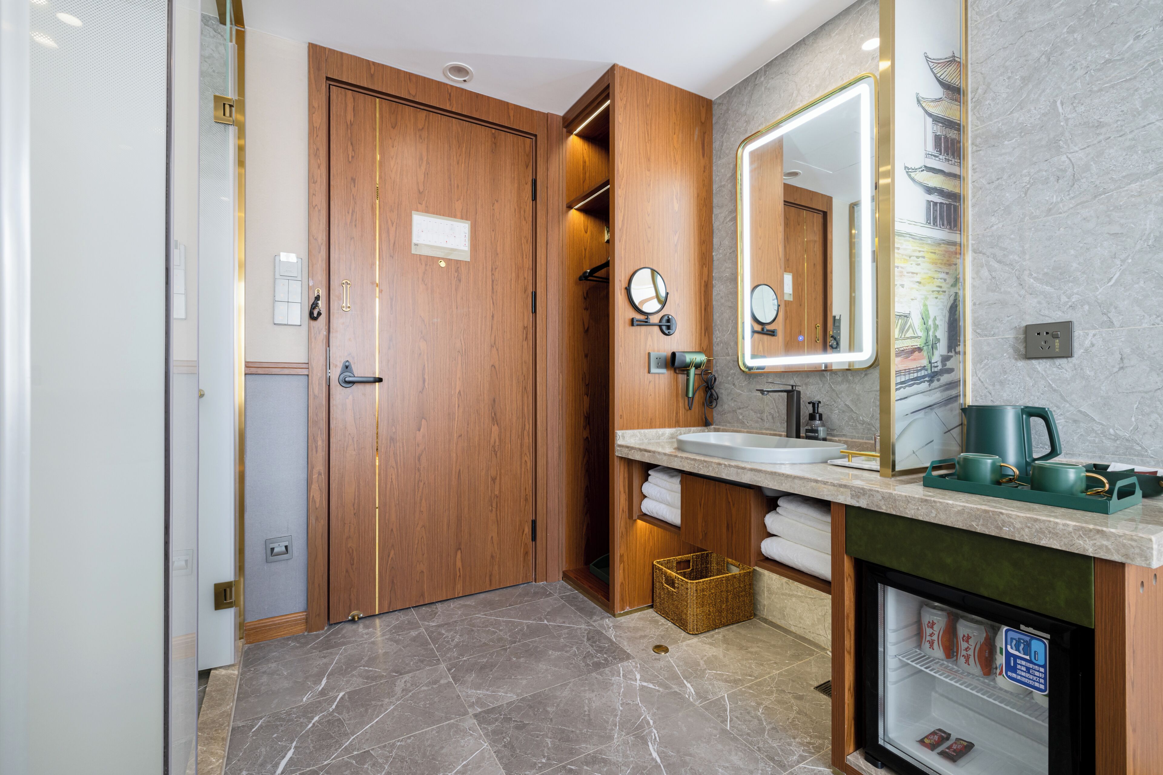 A modern bathroom with a wooden door, a sink with a mirror, and a small refrigerator.