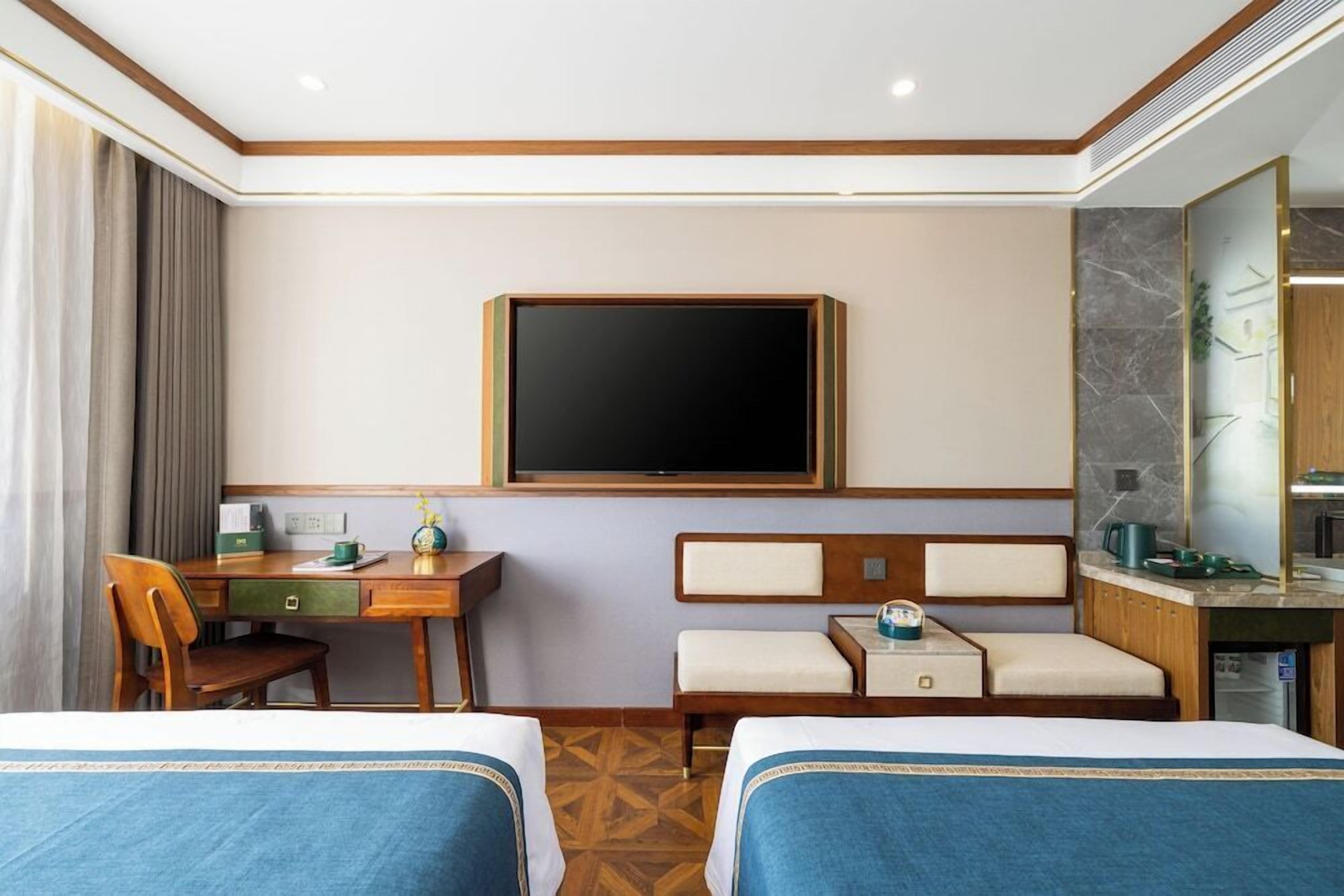 A hotel room with two beds, a desk, a television, and a bathroom.