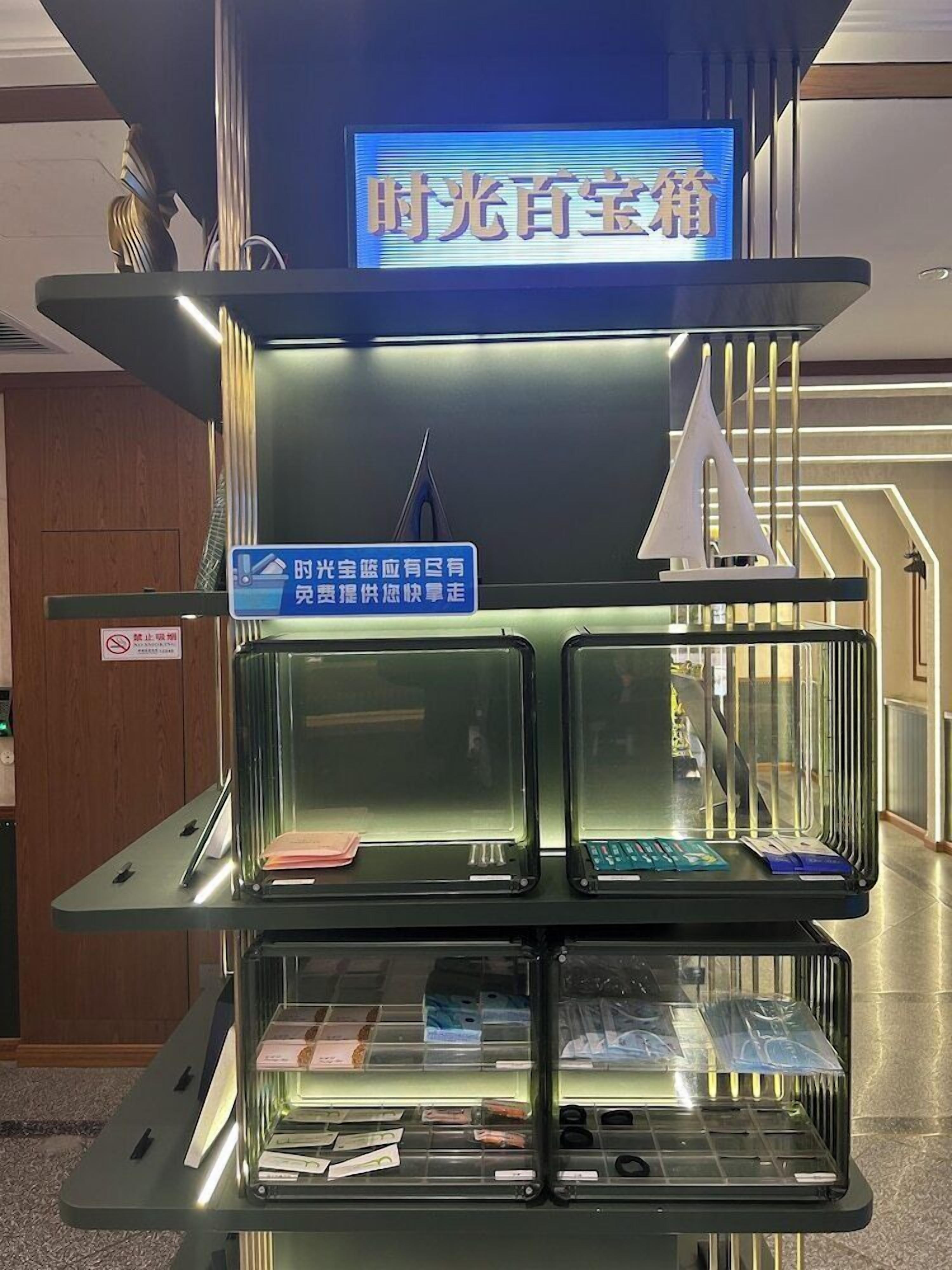A hotel reception area with a digital sign, a glass display case with items, and a sign indicating a free shuttle service.