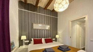 Una camera d'albergo con un letto, due comodini con lampade, uno specchio grande e una porta.
