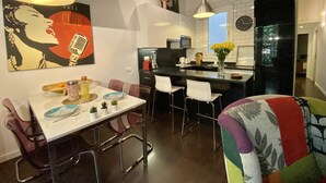 Una cucina moderna con un piano di lavoro nero, mobili bianchi e un'ampia finestra. C'è un'area pranzo con un tavolo e sedie bianche, e una sedia colorata in primo piano.