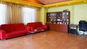 Una sala de estar con dos sofás rojos, una mesa de centro, un aparador de madera con puertas de vidrio y una silla de oficina negra.