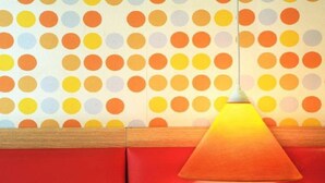 Una habitación con papel tapiz de lunares, un banco rojo y una lámpara colgante cónica.