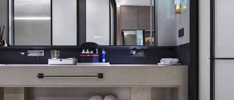 A modern bathroom with a large mirror, a towel rack, a sink, and a shelf with toiletries.