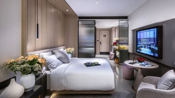 A modern hotel room with a large bed, a TV mounted on the wall, and a small seating area. - Mehood Elegant Hotel Qianjiang (Hangzhou)