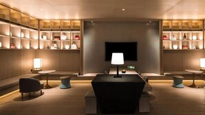 A modern hotel lobby with a central seating area, a flat-screen TV, and shelves with decorative items. - Mehood Elegant Hotel Qianjiang (Hangzhou)