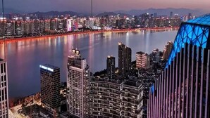 A cityscape at dusk with a river in the foreground and high-rise buildings with illuminated windows. - Mehood Elegant Hotel Qianjiang (Hangzhou)
