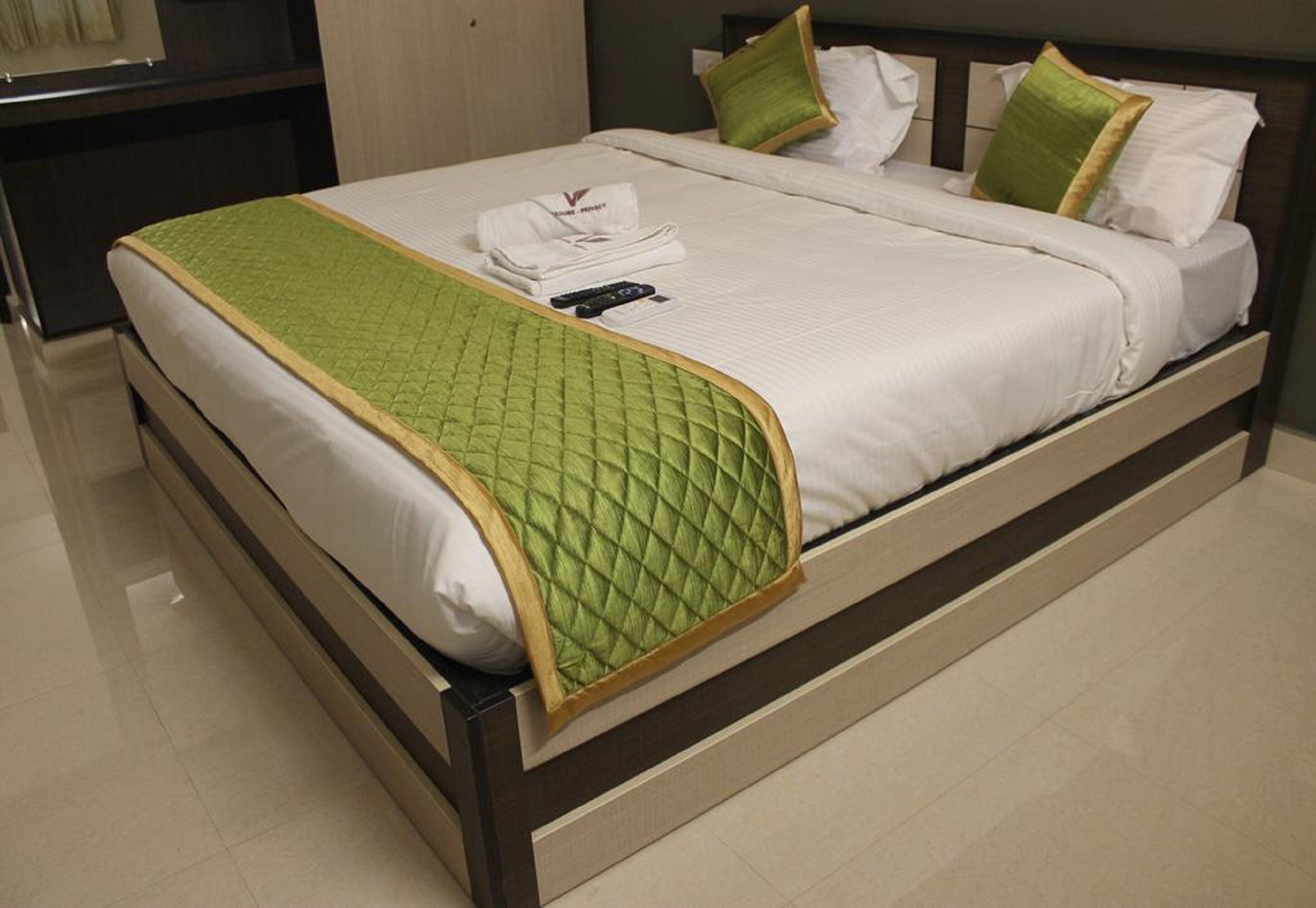 A neatly made bed with a green quilt, white linens, and a remote control on it.